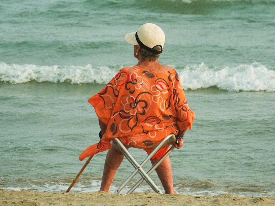 Senior adult sitting on a beach chair gazing at the ocean, enjoying a tranquil summer day.