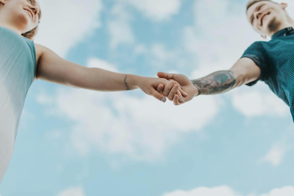 A couple holds hands outdoors, symbolizing love and connection, photographed from a low angle.
