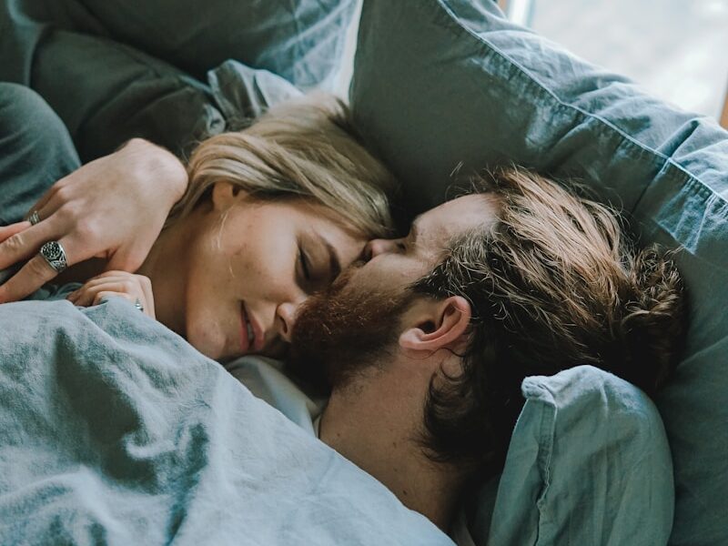 man kissing woman's forehead while lying on bed