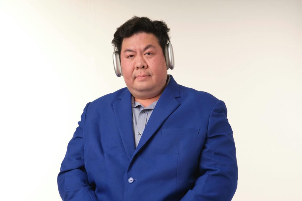 Portrait of a man in a blue suit wearing headphones against a plain background.