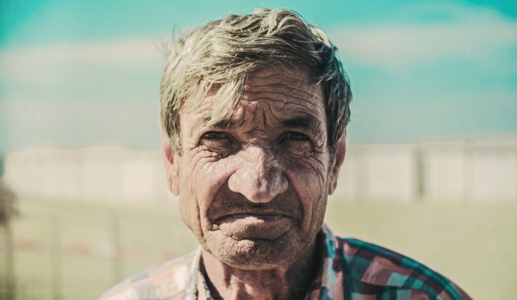 Close-up portrait of an elderly man with wrinkles, outdoors in daylight.