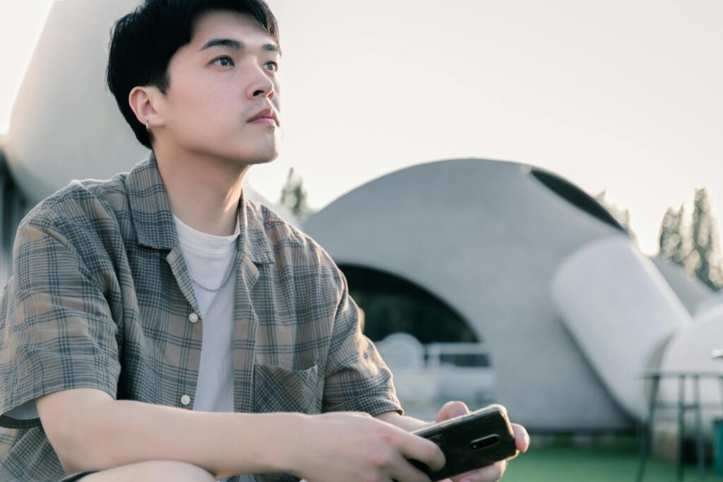 A young man gazes thoughtfully at modern architectural structures in an outdoor setting.