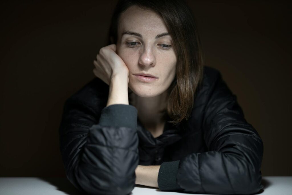 A woman in thought with a serious expression, indoors, in a low-light setting.
