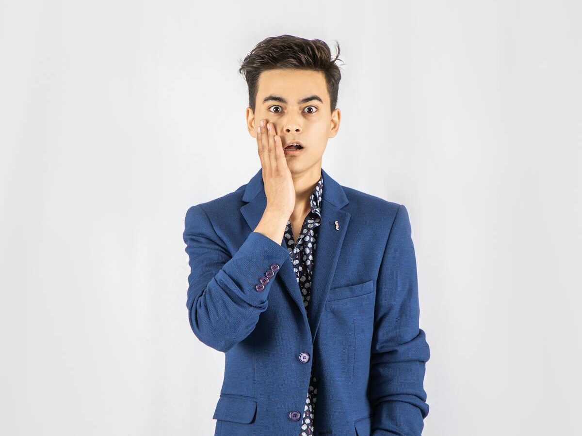 A young man expressing surprise while posing in a blue blazer against a white background.