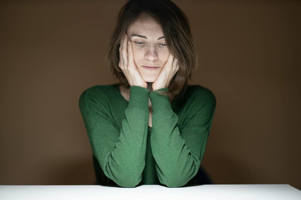 Thoughtful woman in green sweater looking down in low light setting.
