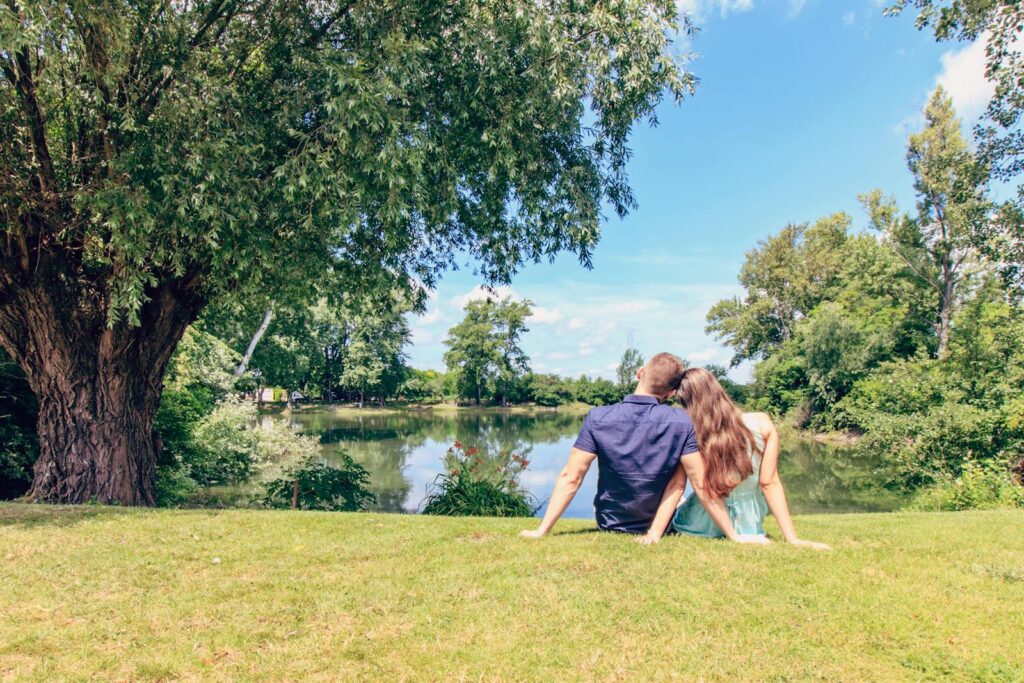 A couple sitting by a lake enjoying a sunny day in a lush park.