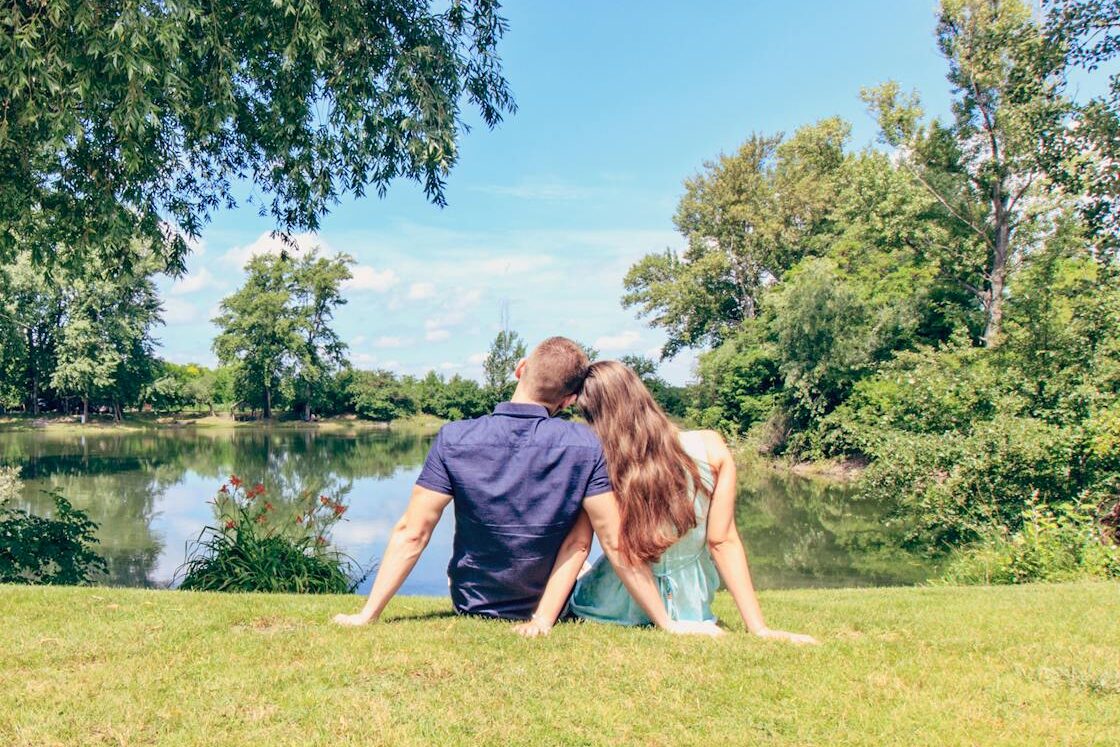 A couple sitting by a lake enjoying a sunny day in a lush park.