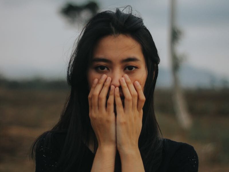 A thoughtful woman stands outdoors in Jember, Indonesia, amid serene natural surroundings.