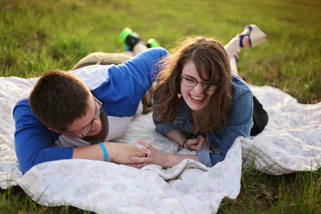 Smiling couple relaxing on a blanket during a sunny day picnic in a grassy field.