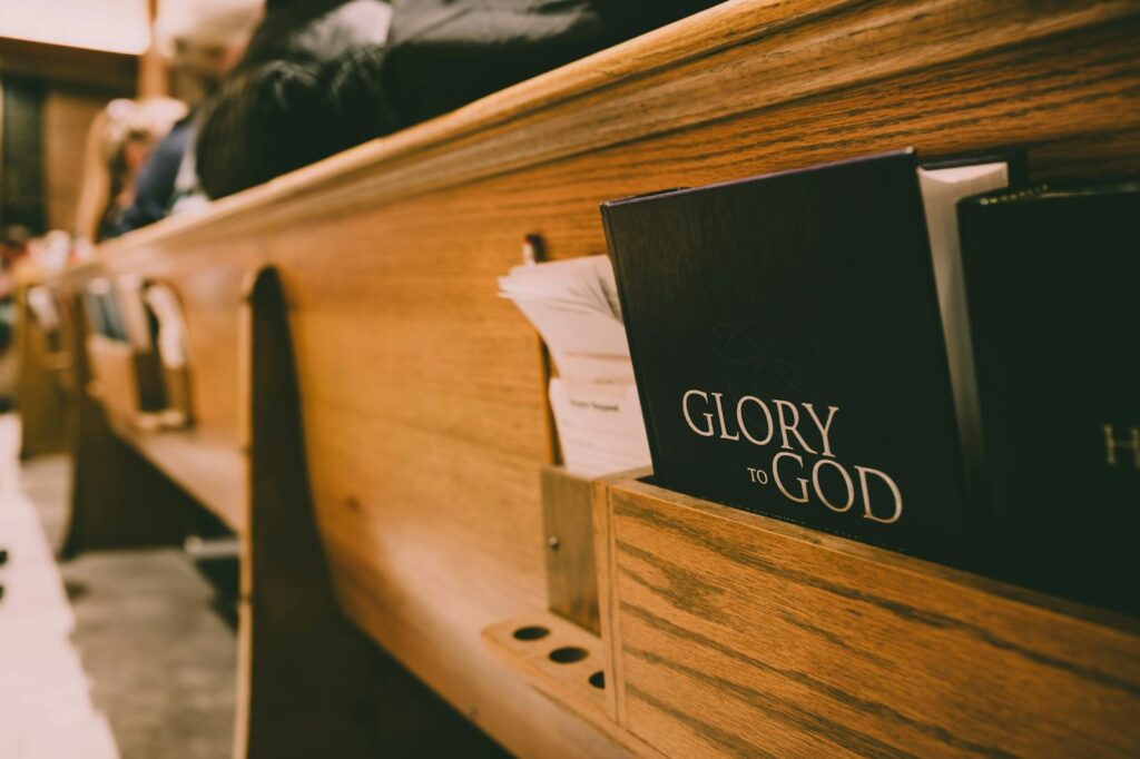 A close-up of a wooden church pew holding hymnals and a Bible, symbolizing worship.