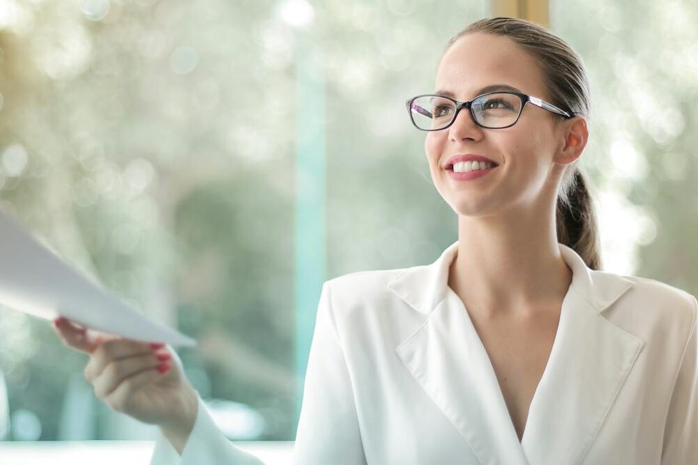 Low angle of successful female executive manager in classy style sitting at table with laptop in contemporary workplace and passing documents to colleague