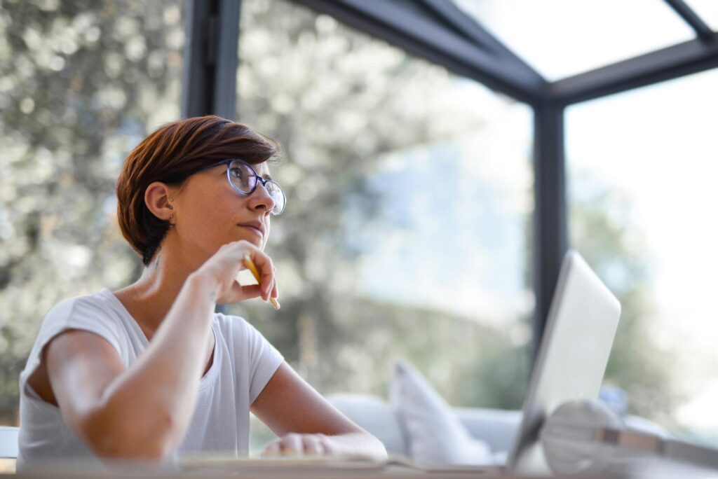 Thoughtful woman with glasses and short hair looking out window in a modern room.