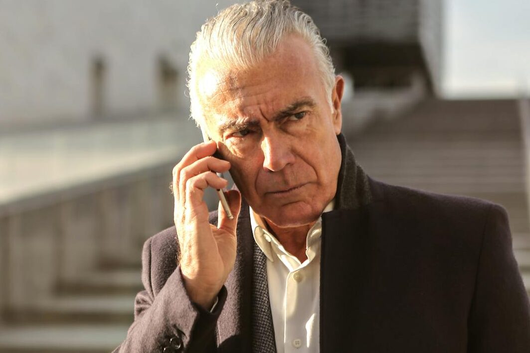 Serious senior businessman using a smartphone outdoors, conveying a professional and pensive mood.
