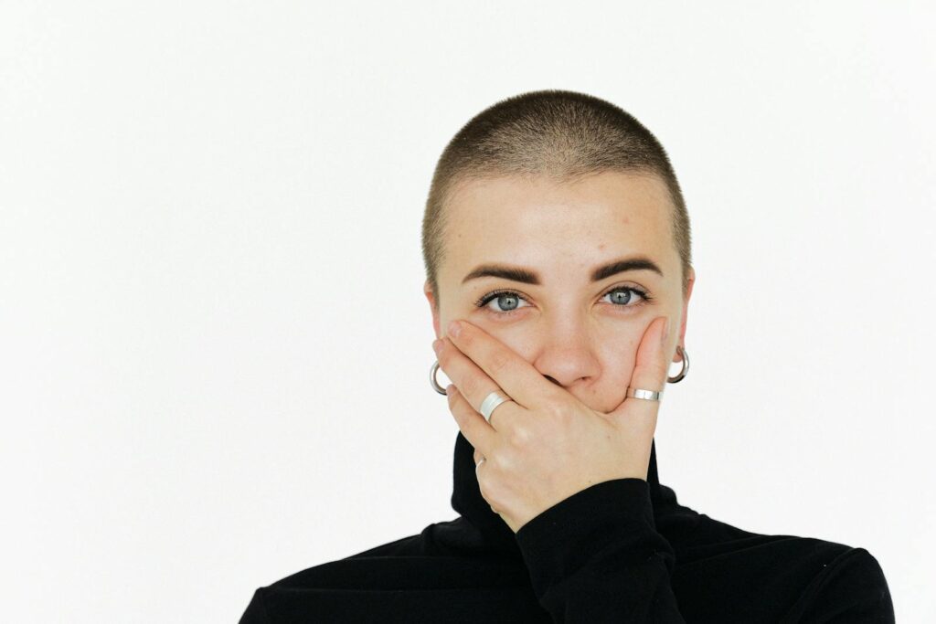 Close-up portrait of a woman with a surprised expression, covering her mouth, on a plain white background.