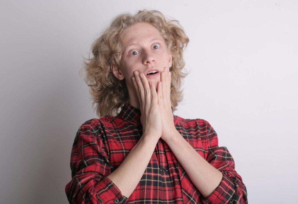 Portrait of a surprised teenage male with curly hair and plaid shirt expressing shock indoors.