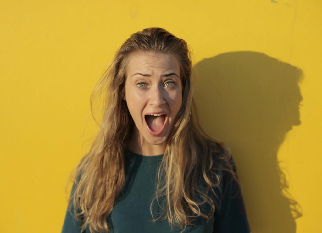 A surprised young woman with long hair against a vibrant yellow background in a studio shoot.
