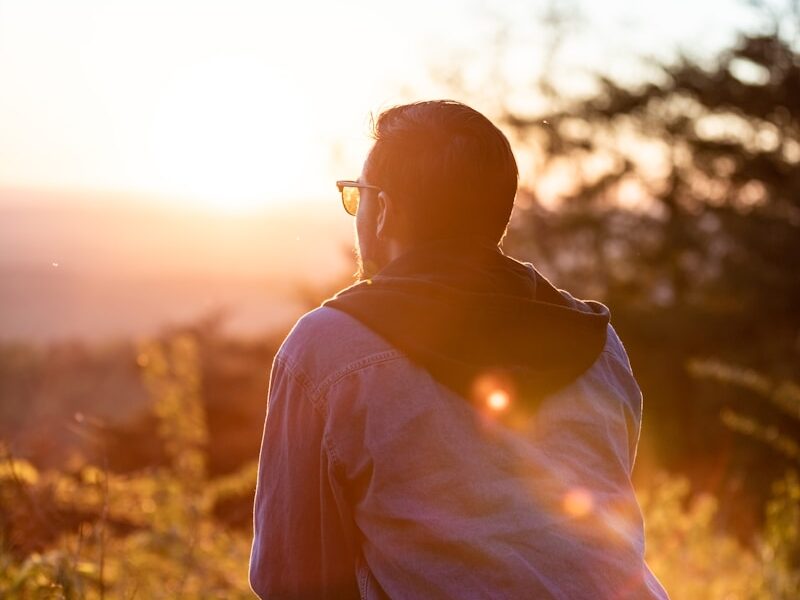 woman in white shirt and sunglasses sitting on brown wooden bench during sunset