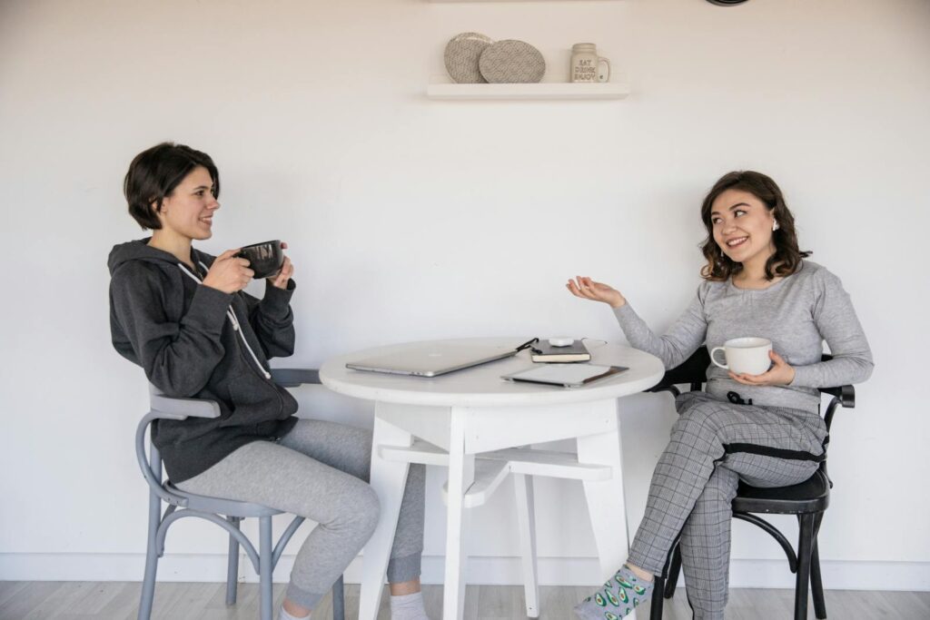 Two women enjoying a friendly chat over coffee indoors, relaxed and smiling.