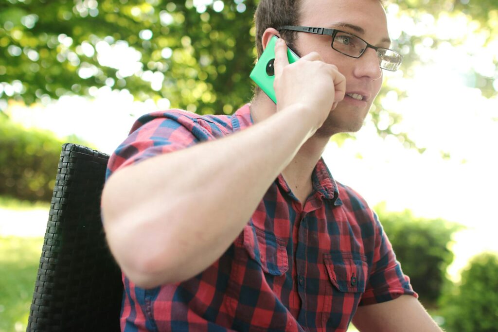 Casual man in plaid shirt having a phone conversation in a sunny park setting.