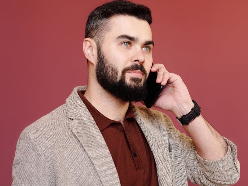 Professional man in a brown coat using smartphone against red background.