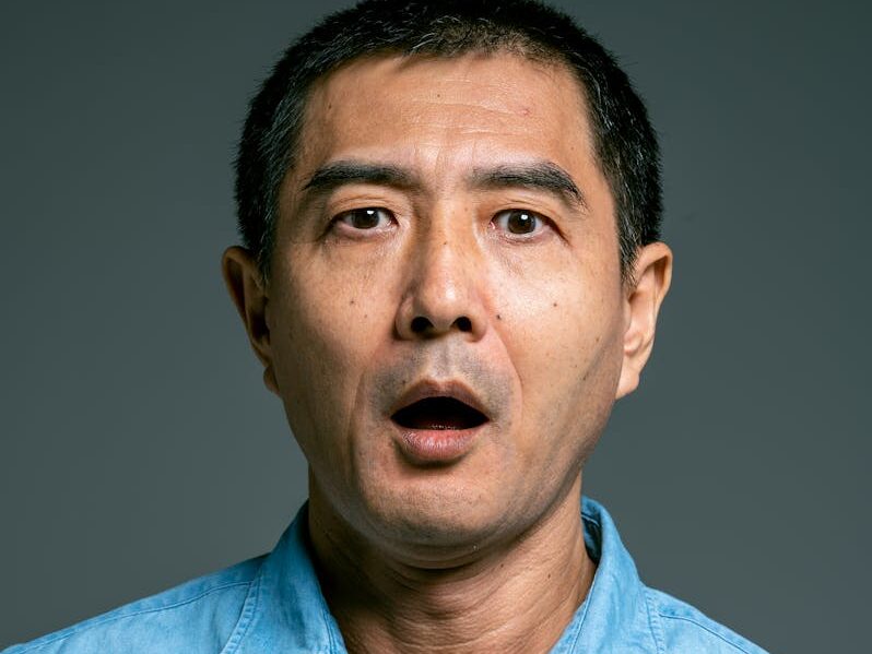 Close-up of a surprised man with open mouth wearing a blue denim shirt.