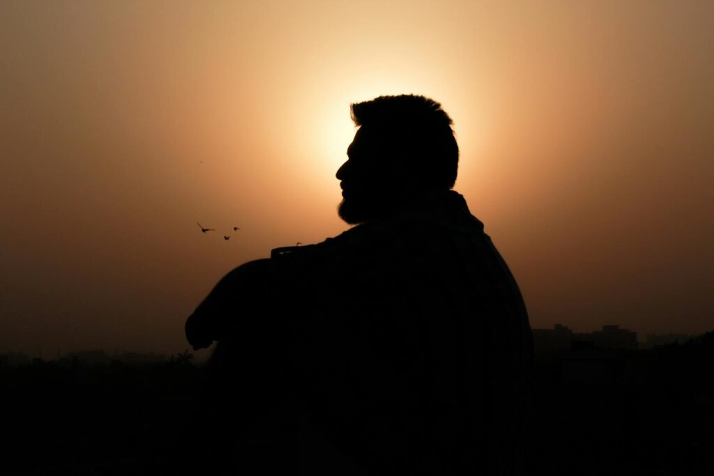 A silhouette of a man sitting in profile against a stunning golden sunset, creating a peaceful and reflective scene.