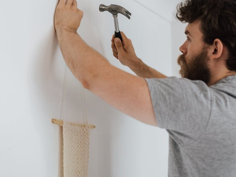 Man using a hammer to hang a decoration on a wall indoors.