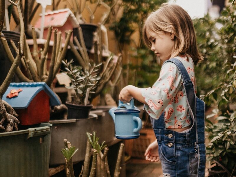 girl wearing blue romper holding teal watering can