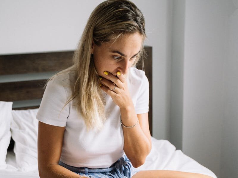 Young woman sitting on bed, concerned expression while using a laptop indoors.