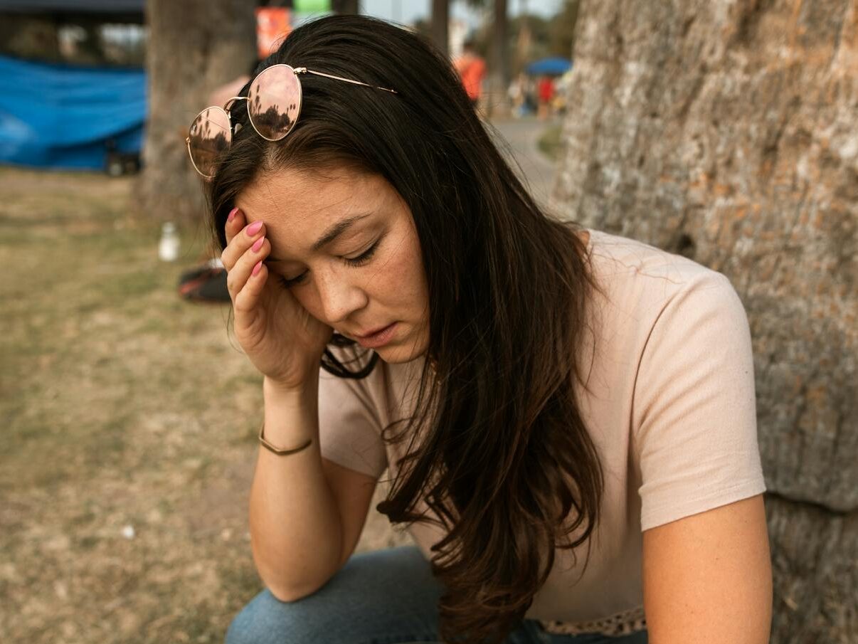 An anxious woman outdoors touching her forehead, showing stress and mental exhaustion.