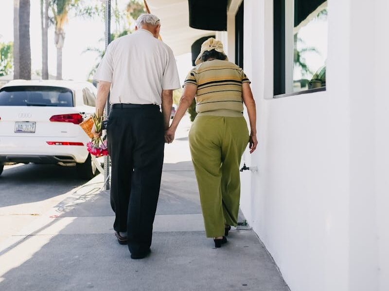 Senior couple holding hands walking together outdoors on a sunny day, showing love and companionship.