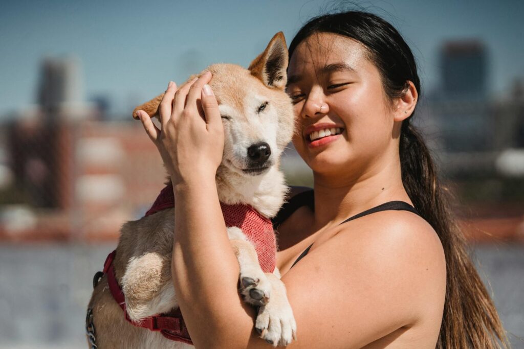 A happy woman embraces her fluffy dog in a sunny outdoor setting, showcasing their strong bond.