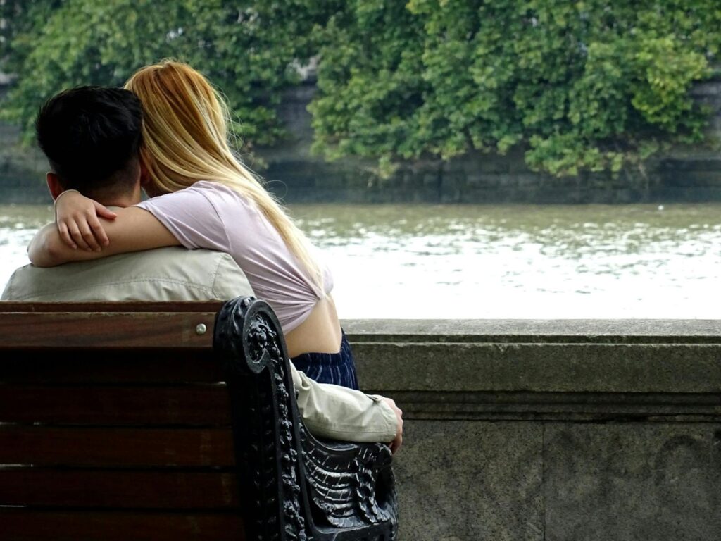 Young couple sharing a tender moment on a park bench by the riverside