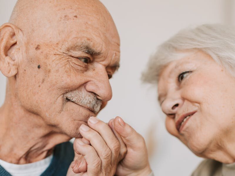 An elderly couple expressing love and affection, holding hands indoors.