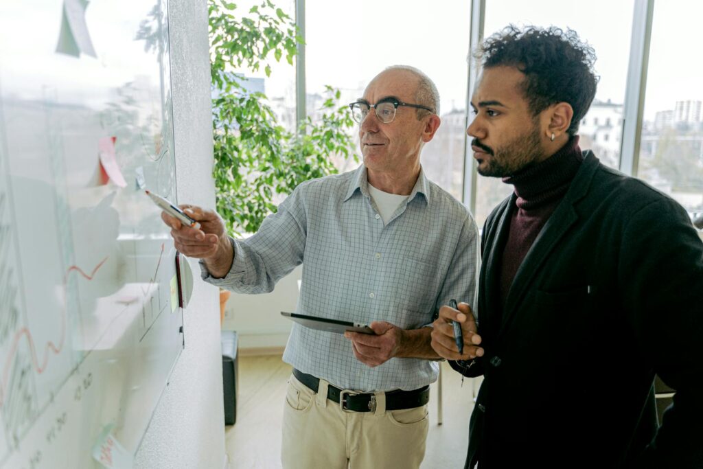Two business professionals in discussion while collaborating at a whiteboard in a modern office.