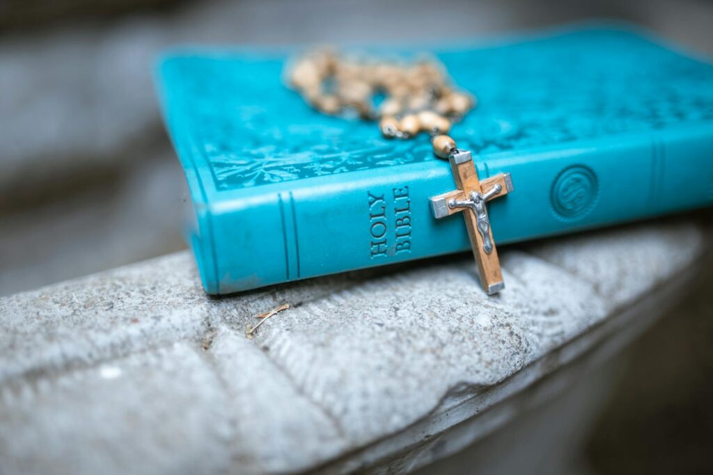 A teal Holy Bible with a rosary resting on a marble surface, symbolizing faith and devotion.