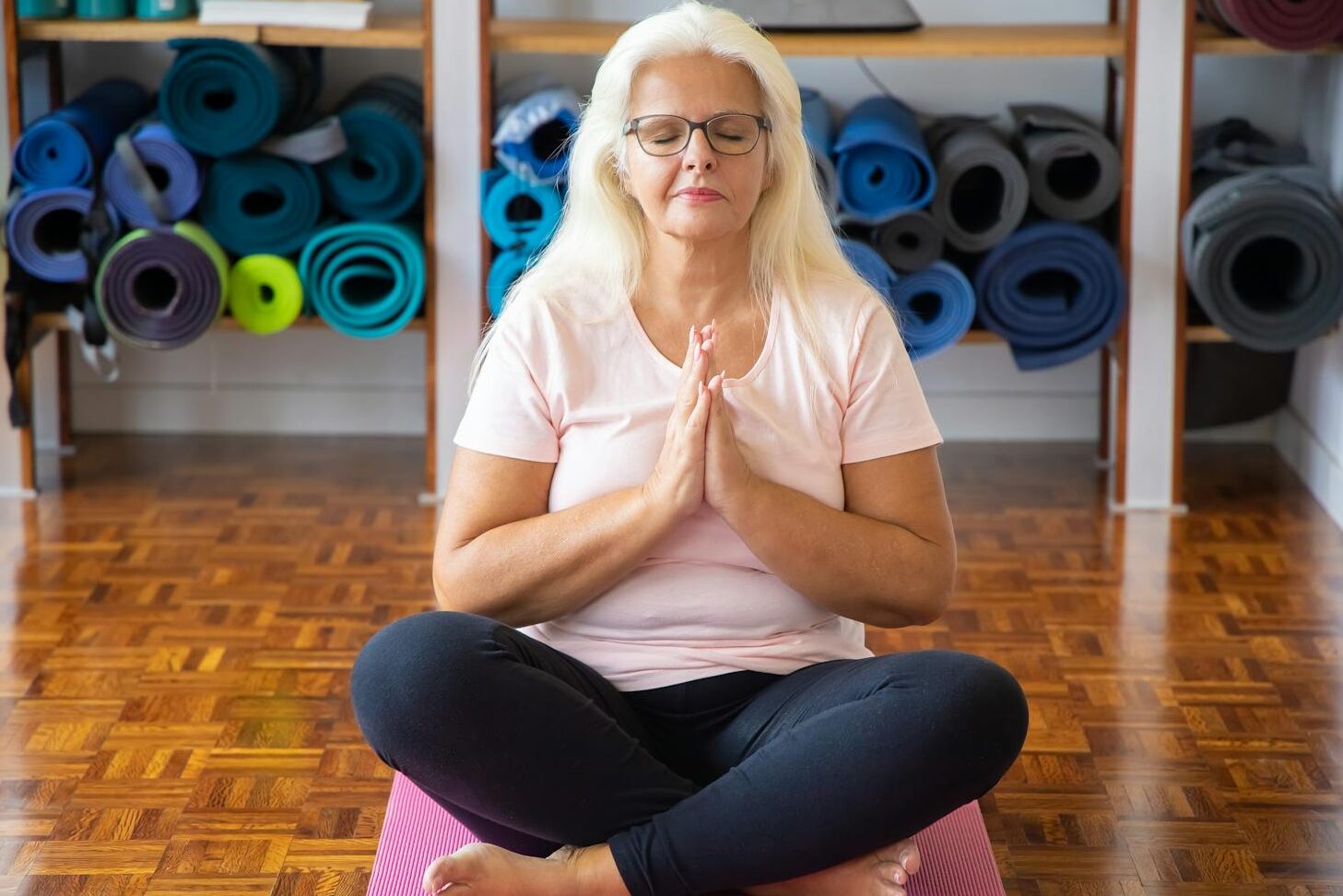 Senior woman meditating on yoga mat, promoting relaxation and wellness indoors.