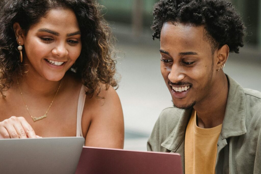 Two young adults happily collaborating on laptops outdoors, enjoying technology.
