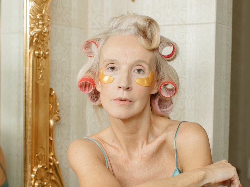 A senior woman in hair rollers practicing her skincare routine, sitting elegantly in a vintage bathroom.
