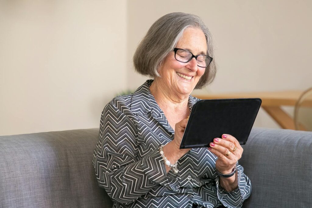 Happy senior woman with gray hair using a tablet at home, enjoying technology.
