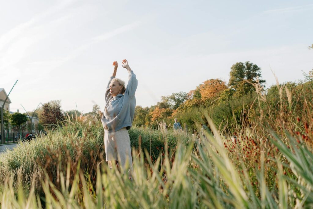 Senior woman enjoying stretching exercises in a lush green park.