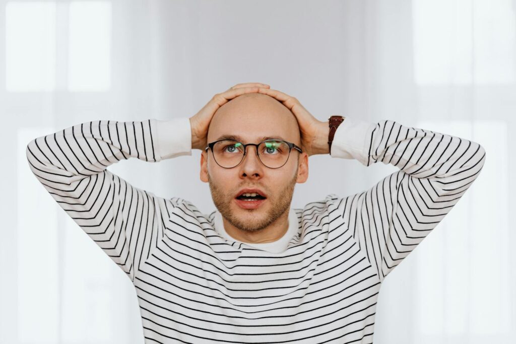 Bald man in striped shirt holding head in surprise indoors.