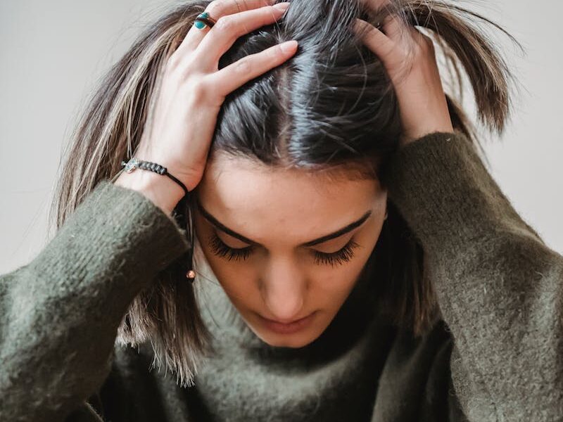 A woman sitting indoors, appearing stressed or upset, touching her head.