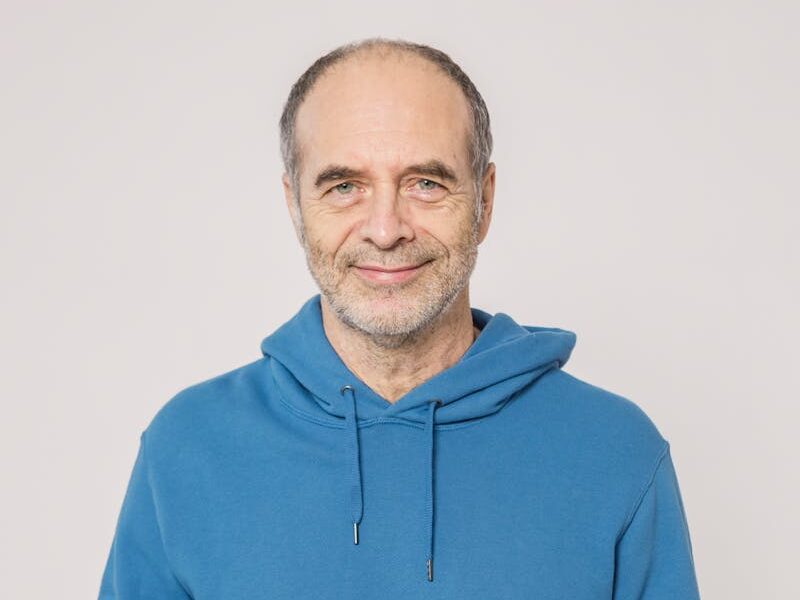 Senior adult in blue hoodie reading newspaper while holding a coffee cup indoors.