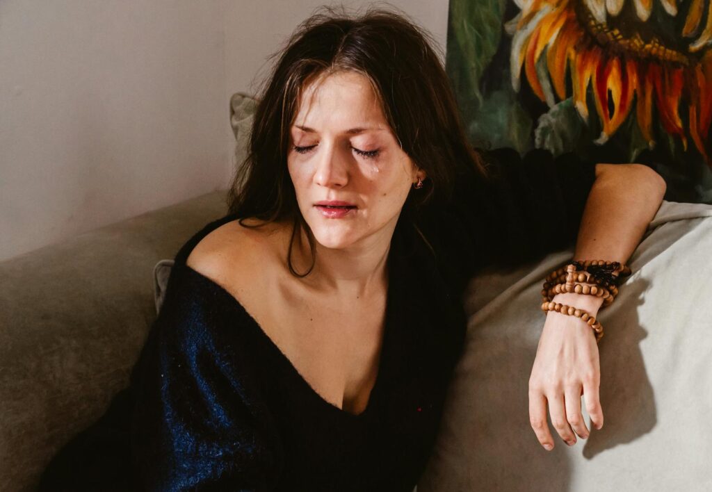 A woman sitting on a couch, eyes closed, expressing deep emotion and contemplation.