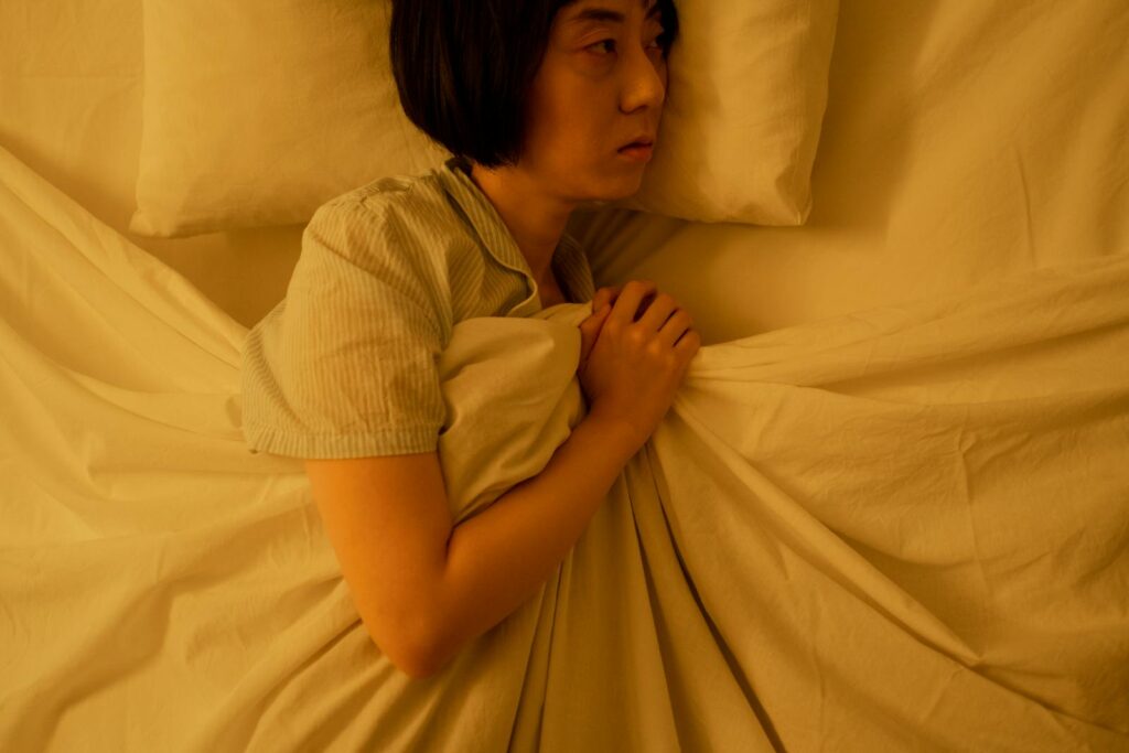 Side view of an Asian woman lying in bed, reflecting anxiety and insomnia in dim light.