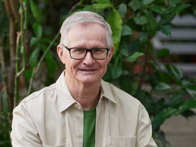 Elderly man enjoying remote work on a laptop in a garden setting.