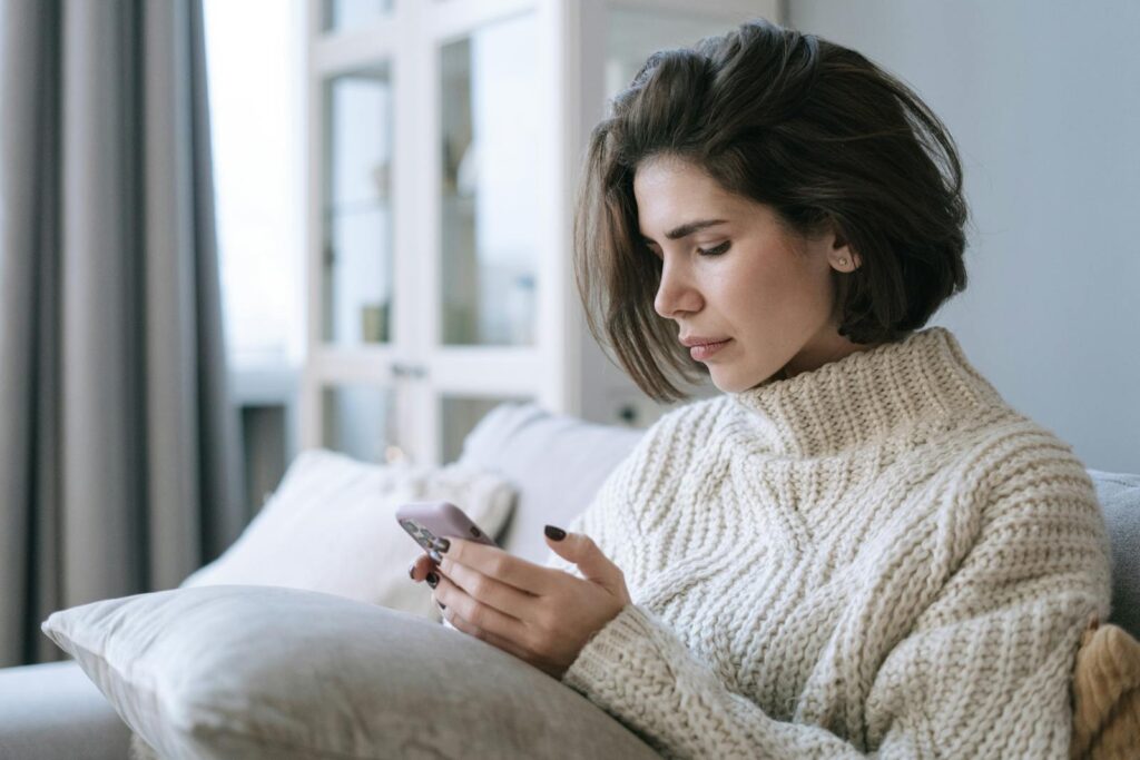 A Woman in White Knitted Sweater Using a Cellphone