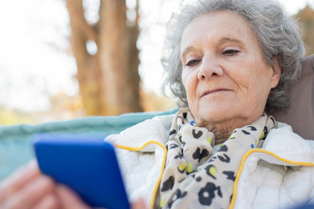 Elderly woman with a smartphone relaxing outdoors in autumn.
