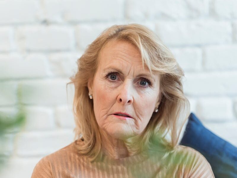 Serious elderly female in clothes with striped ornament looking at camera while sitting on sofa at home